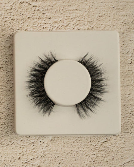 Pair of false eyelashes on a white card next to a brown box with 'Adelaide' branding on a beige background