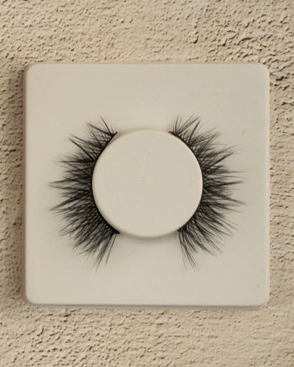 Eyelash packaging with a cardboard box and a white card displaying false eyelashes on a textured beige background.